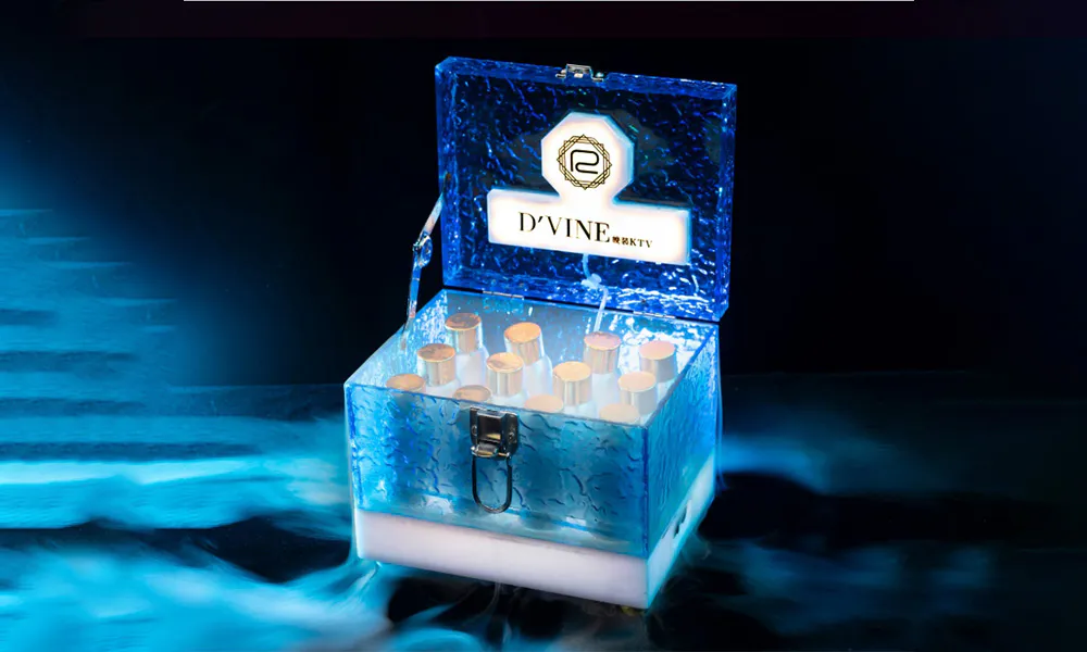 Transparent glowing blue ice-texture D'VINE liquor chest, with logo on lid, filled with mini gold-cap bottles, smoky mist at base