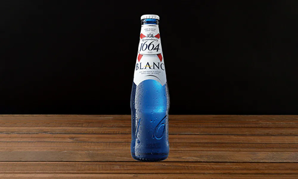 One bottle of 1664 Blanc wheat beer on wooden table, blue glass covered with condensation drops, solid black background