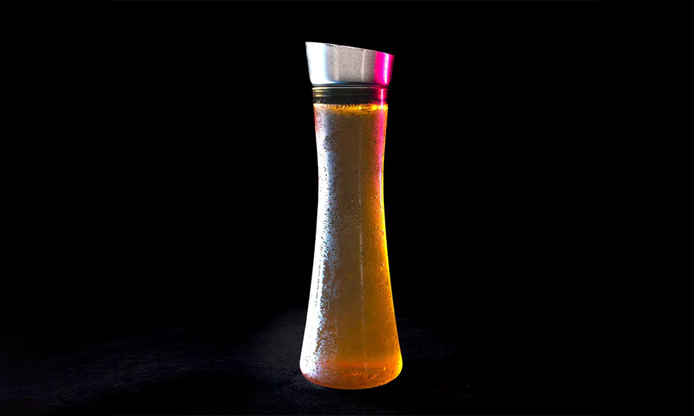 Waisted glass pitcher covered with condensation, filled with orange drink, metal angled lid, black background with pink-purple neon glow.